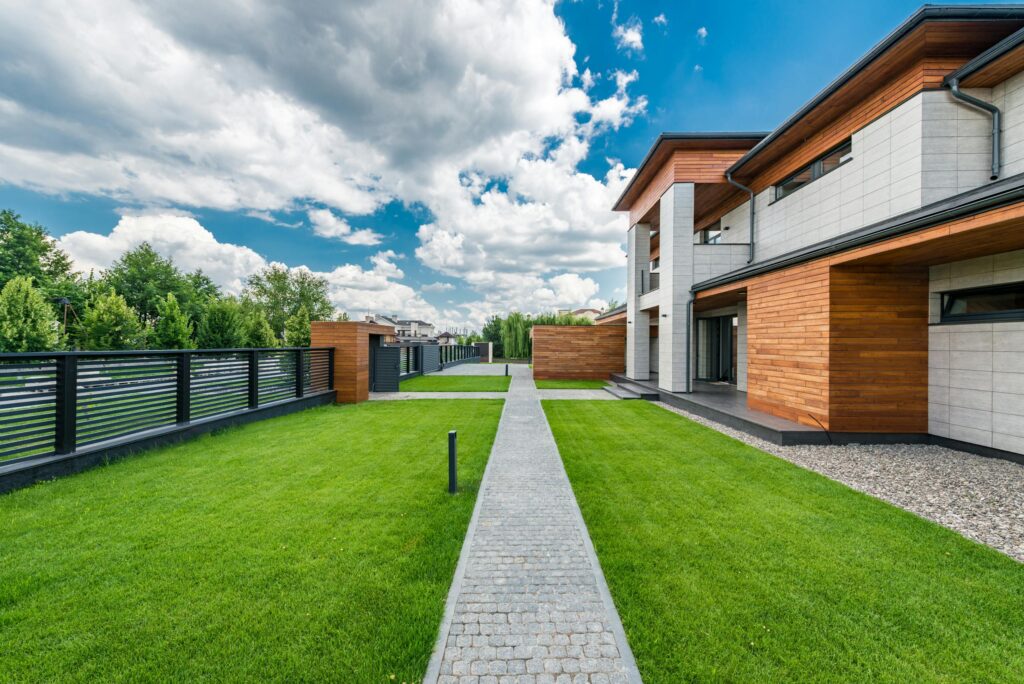 A modern house exterior with contemporary design, lush green lawn, and blue sky offering a tranquil and scenic view.